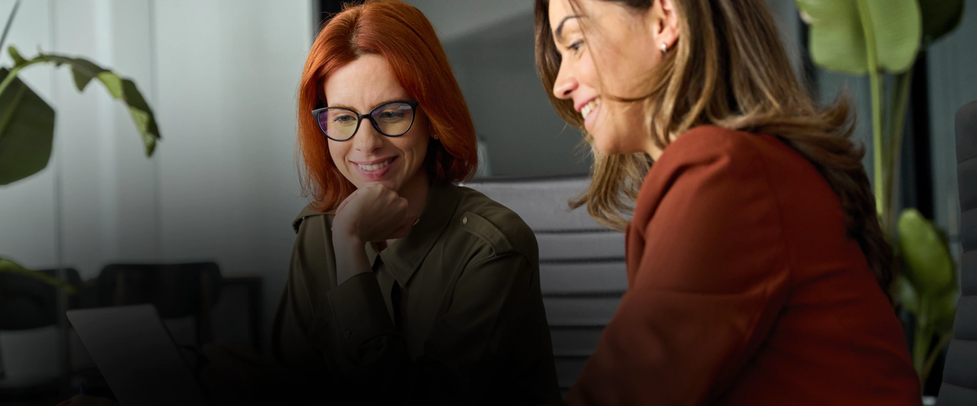 Dwie uśmiechnięte kobiety, siedzące przy stole konferencyjnym.