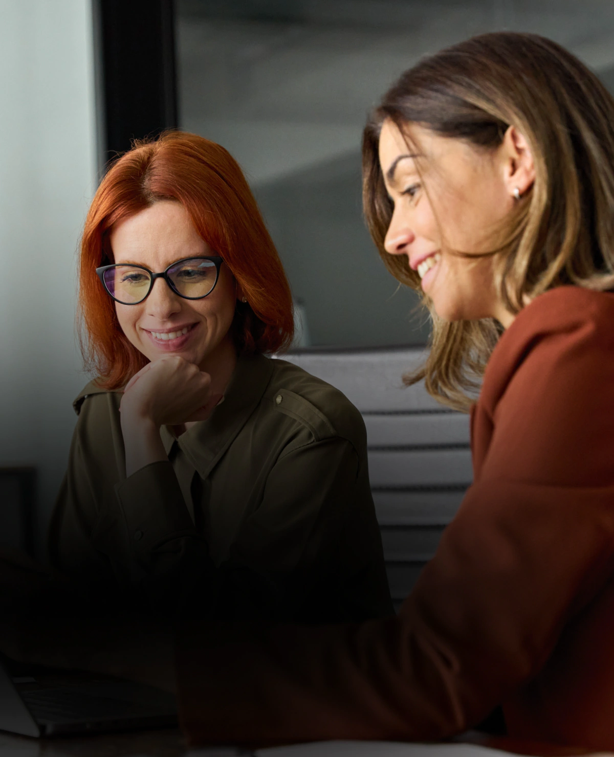 Dwie uśmiechnięte kobiety, siedzące przy stole konferencyjnym.