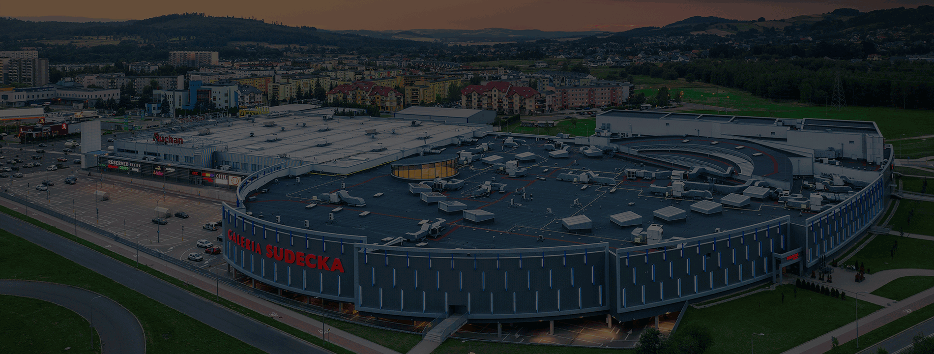 Widok z lotu ptaka na budynek Galerii Sudeckiej z piekną panormą w tle i zachodzącym słońcem.